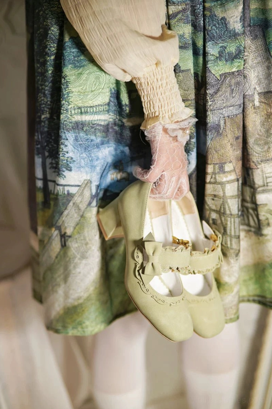 Sage green lolita chunky heel mary jane shoes with double bow and ruffled strap trim in suede material, low front view of held shoes worn with vintage print skirt and ruffled lace gloves