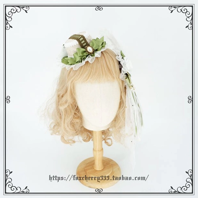 Sage green Lolita mini top hat headdress worn on mannequin head with blonde wig featuring ruffled trim pearl brooch and white lace accents