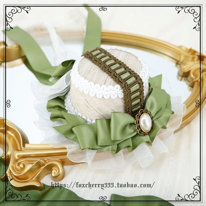 Sage green Lolita mini top hat headdress showing linen-style hat body scalloped lace trim and pearl brooch details on vintage golden mirror prop