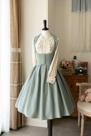 Sage green vintage retro classic lolita JSK jumper skirt with cream blouse, soft muted fabric, front button trim detail, ruffled stand collar, full pleated skirt silhouette, displayed on mannequin in cozy vintage bedroom backdrop