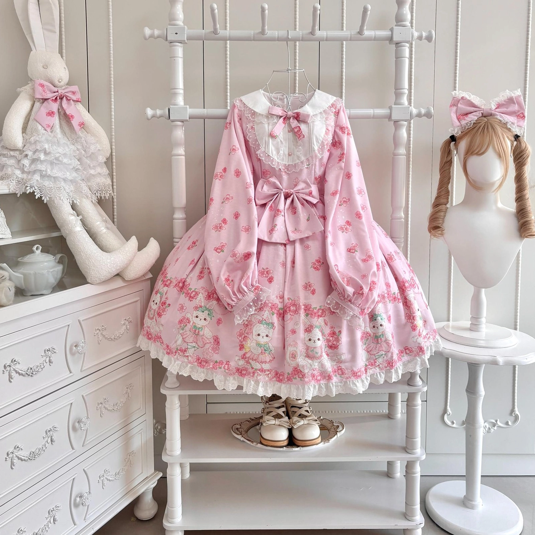 Baby pink Sakura Bunny Lolita OP dress side front view on mannequin with twin-tail styling displaying matching cherry blossom print puffed long sleeves and lace trim with matching KC hair accessory