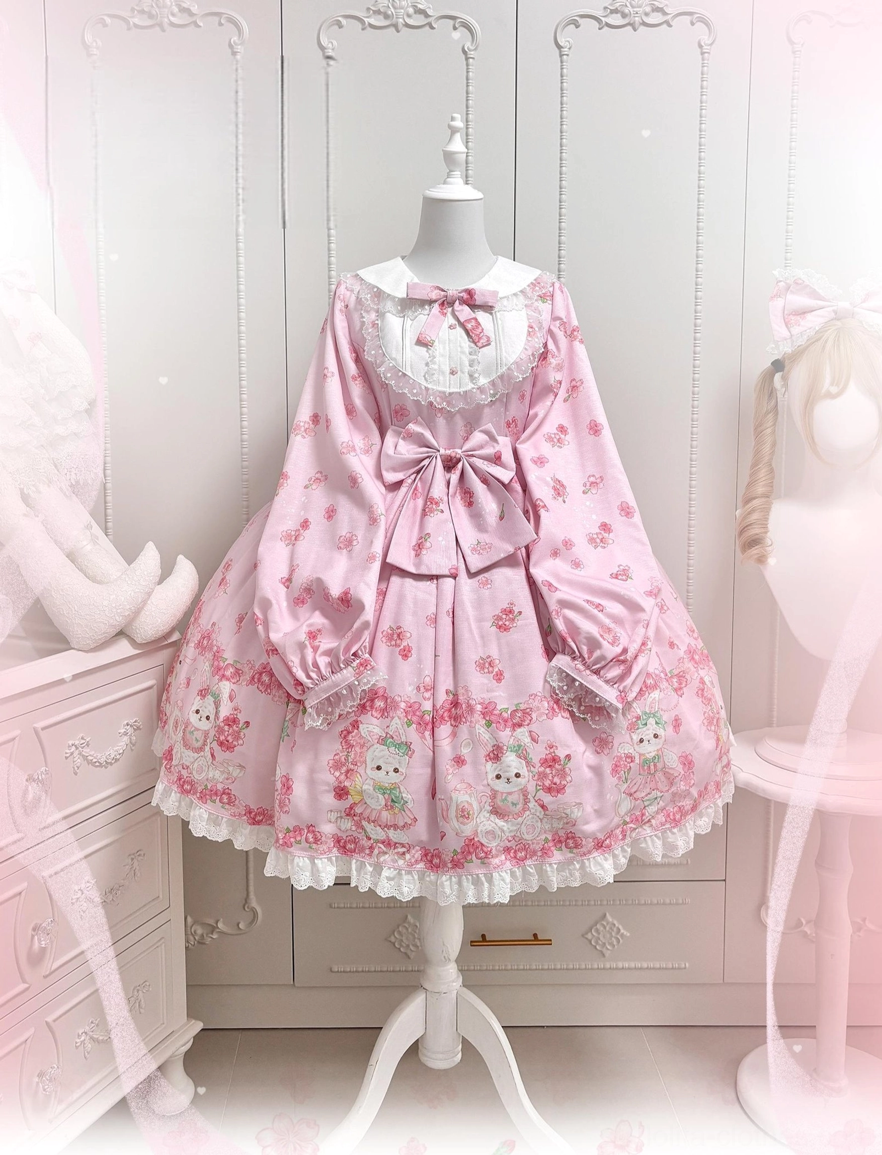 Baby pink Sakura Bunny Lolita OP dress front display on mannequin showing full cherry blossom floral pattern lace ruffled hem Peter Pan doll collar with small bow and large front waist bow