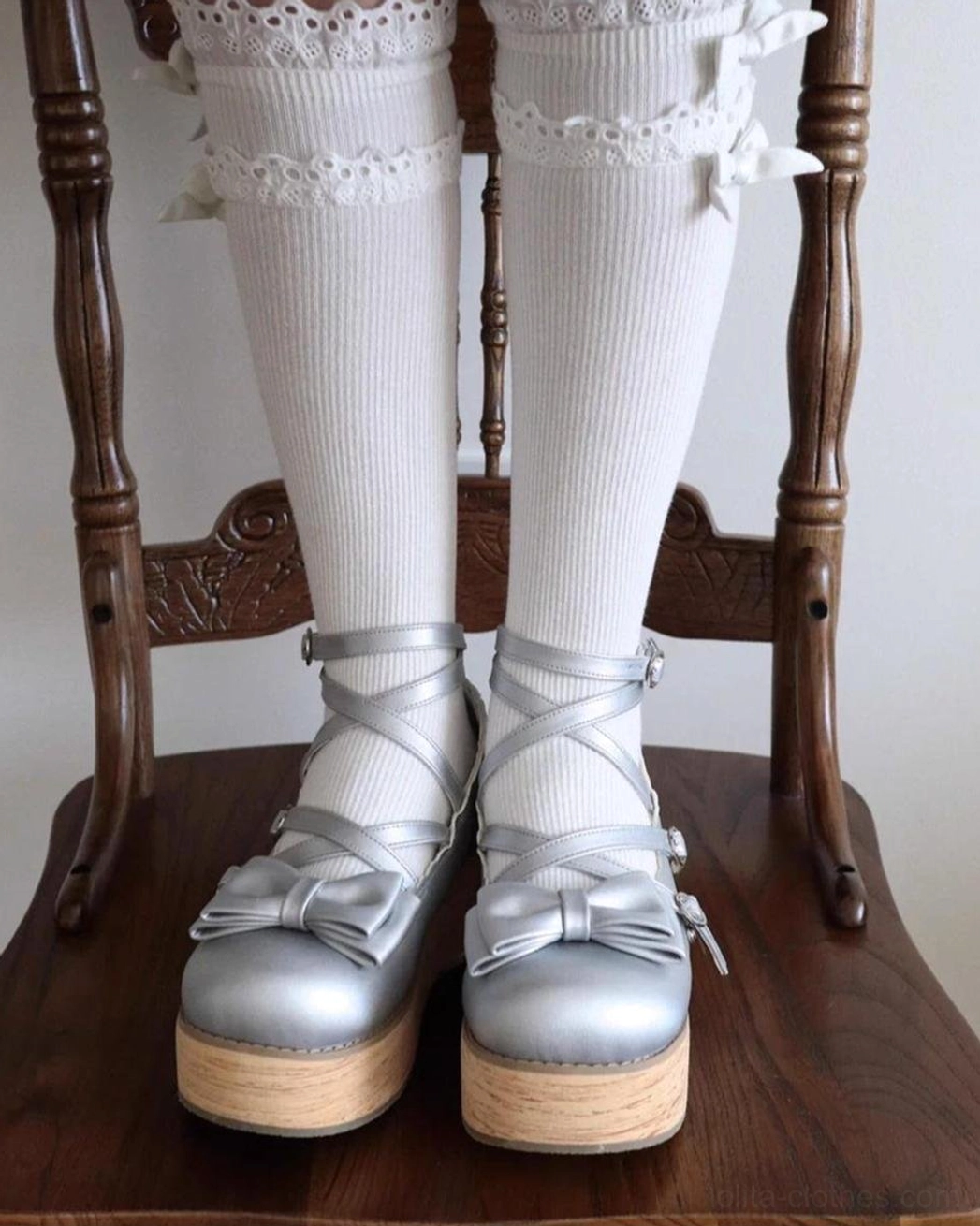 Silver lolita platform shoes low angle close up feet sitting wooden chair white ruffled socks metallic leather bow ankle straps thick platform sole detail