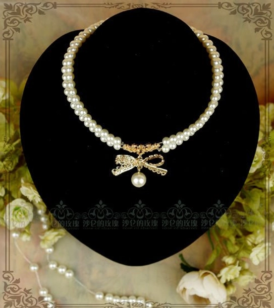 Single-layer pearl chain bow lolita choker necklace front display on black jewelry mannequin with white pearl strand and golden bow charm dangling pearl, vintage floral frame background, jewelry display