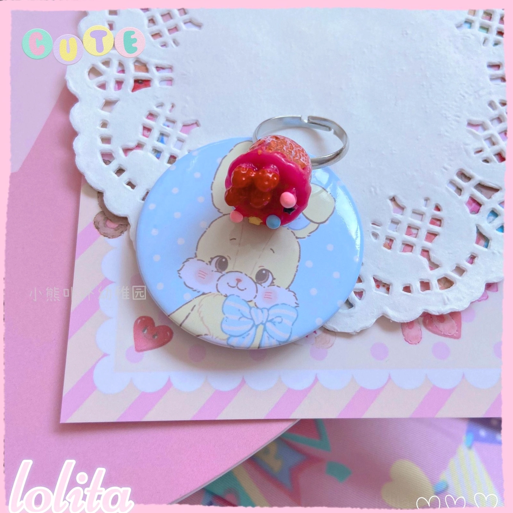 Single glossy red cupcake lolita ring with decorative bead sprinkles and metal base paired with bunny enamel badge on pink striped card