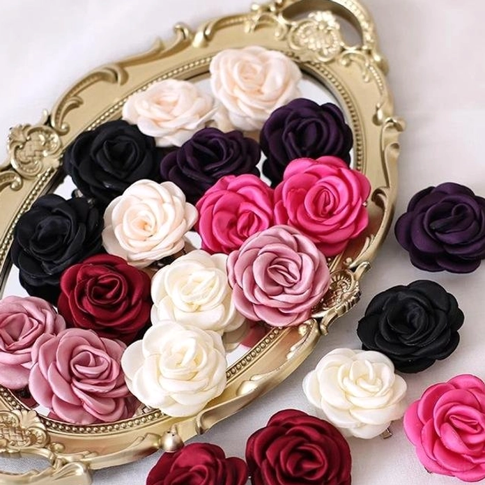 Six distinct color fabric rose brooches and hair clips arranged on ornate golden decorative tray against plain white backdrop