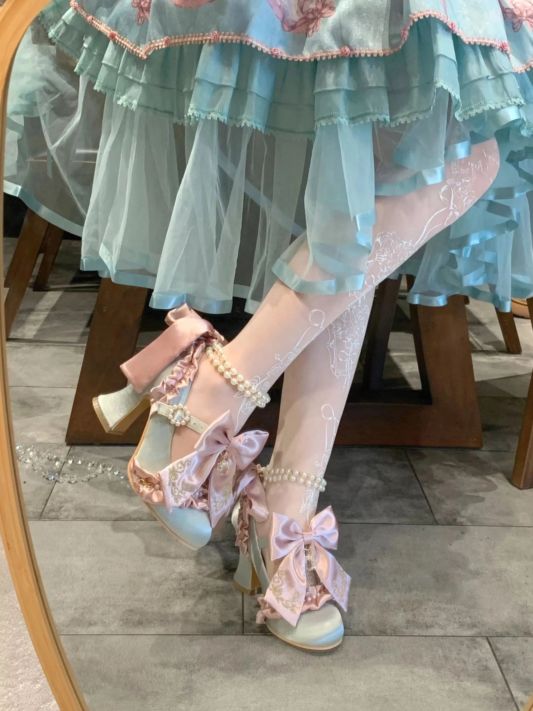 Sky-blue Classic Lolita block heel shoes with pink satin bow and pearl ankle strap, mirror side view worn with sky-blue ruffled tiered Lolita skirt