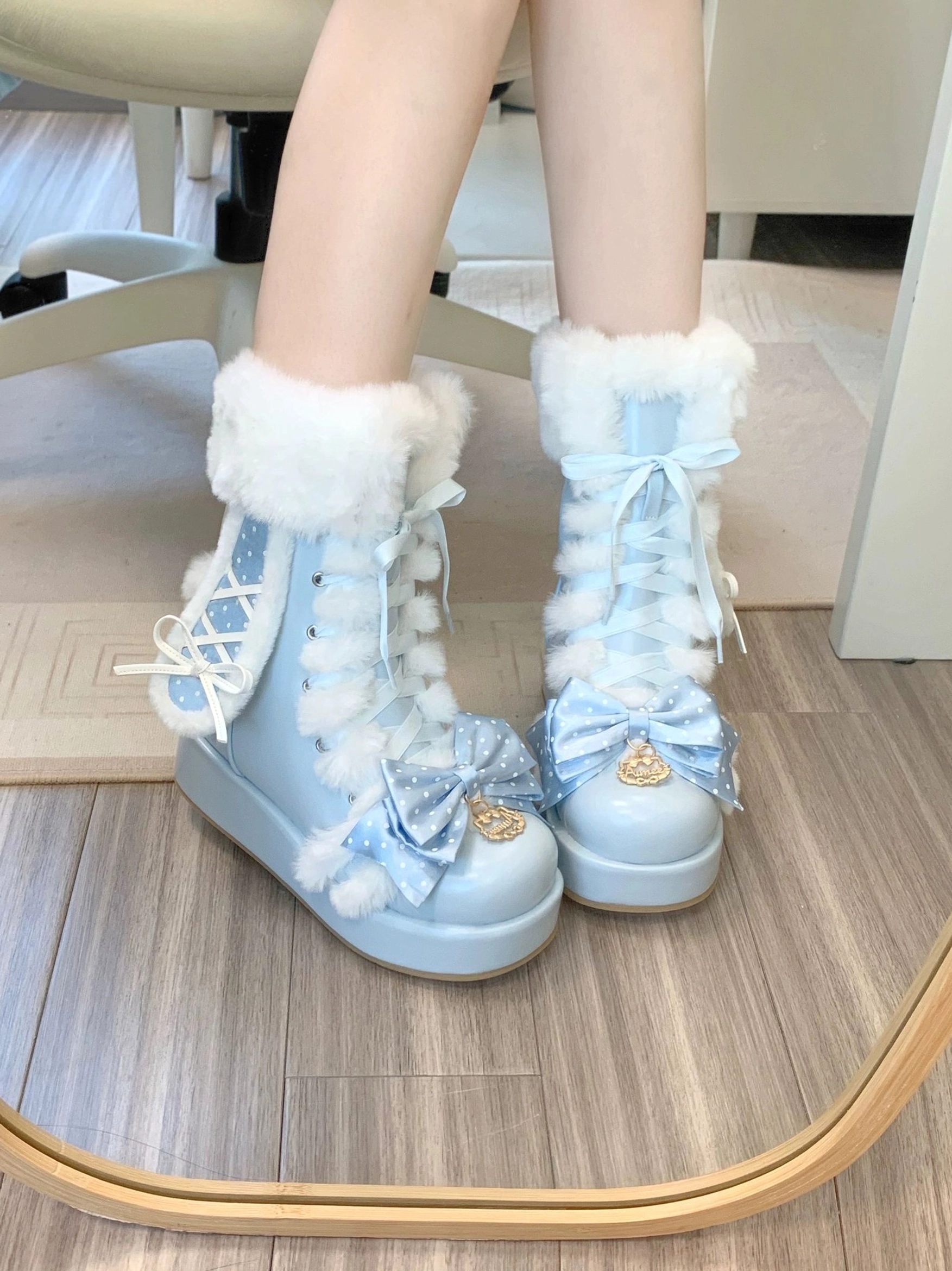 Side view of sky-blue fluffy bunny ear platform boots on model's legs with mirror background, featuring white fur collar, front lace-up closure, large polka dot bow, and elevated platform sole