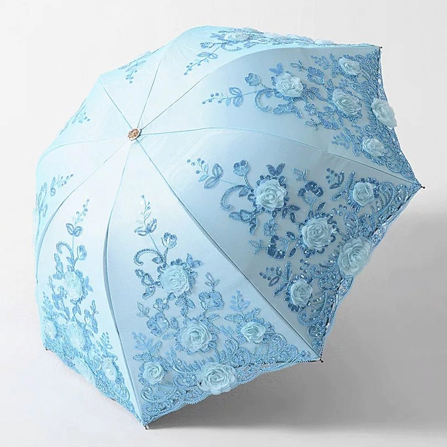 Sky blue foldable lolita floral parasol with blue three-dimensional roses and floral embroidery, matching scalloped lace trim, golden metal center button and handle, fully opened from three-quarter top view against studio white background