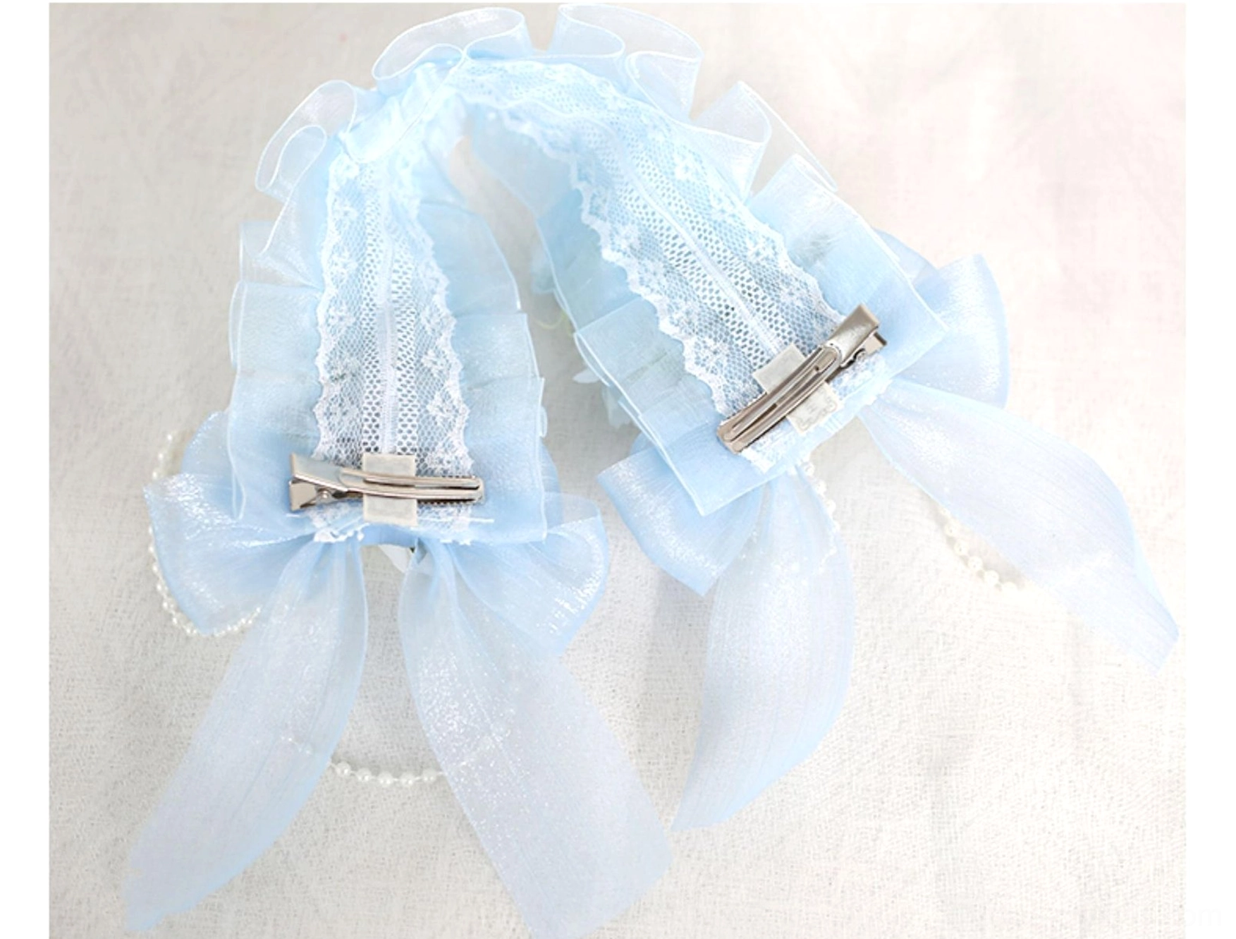 Pair of sky blue lolita lace hair accessories flat lay top-down view with sheer blue bows pearl decorations and metal fixing clips