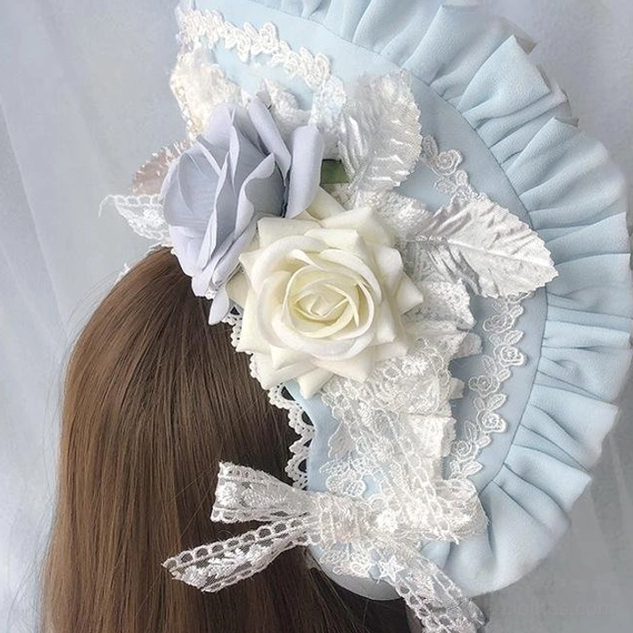 Back side close-up view of sky blue rose-decorated sweet Lolita BNT bonnet with ruffled brim, white lace, cream and gray artificial roses, silver leaf ornaments, and lace bow accent on brown hair mannequin