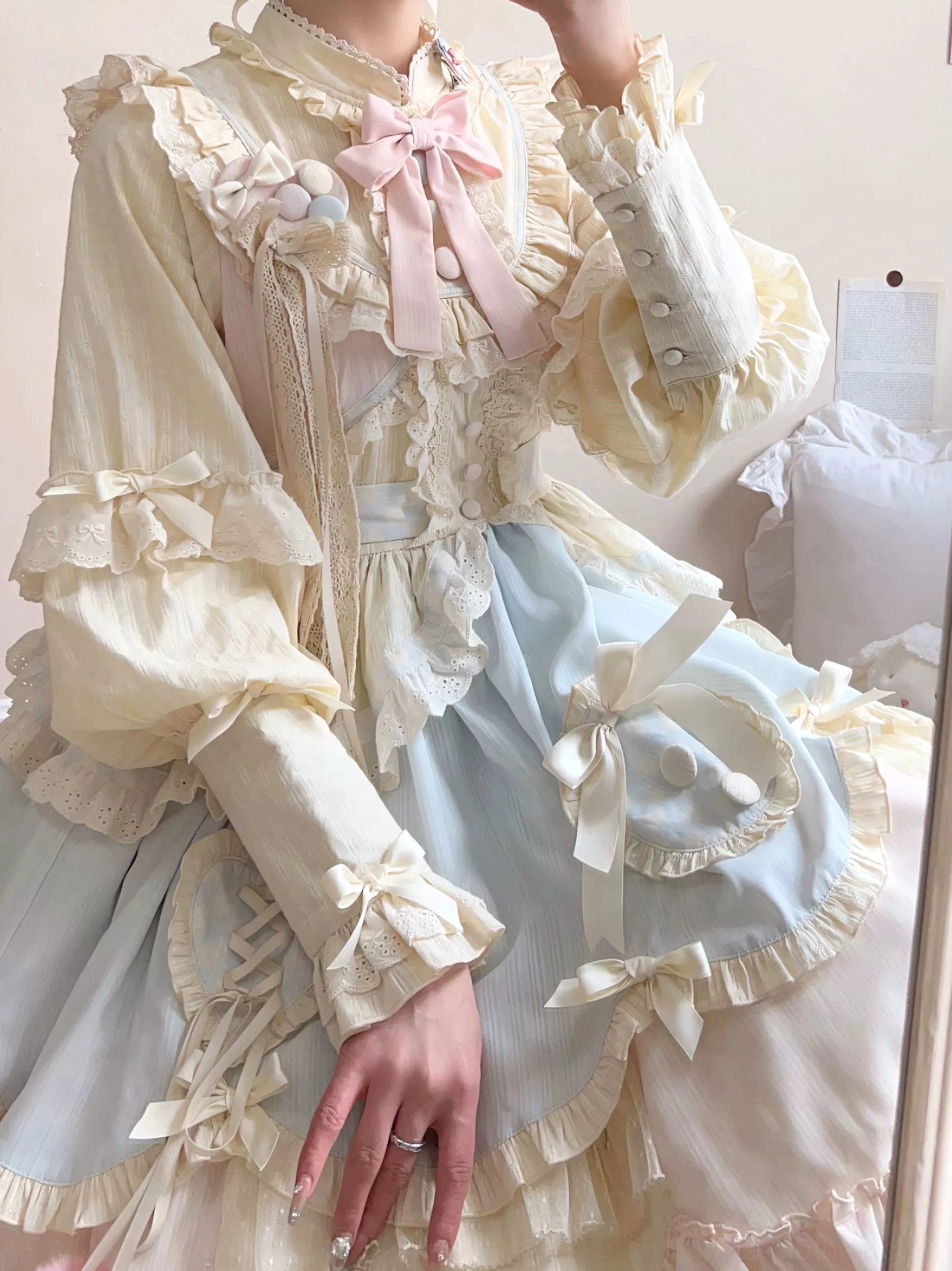 Upper body close-up detail of sweet lolita OP dress showing ruffled lace collar with pink bow tie cream-yellow striped blouse fabric puffed sleeves with lace cuffs decorative fabric buttons