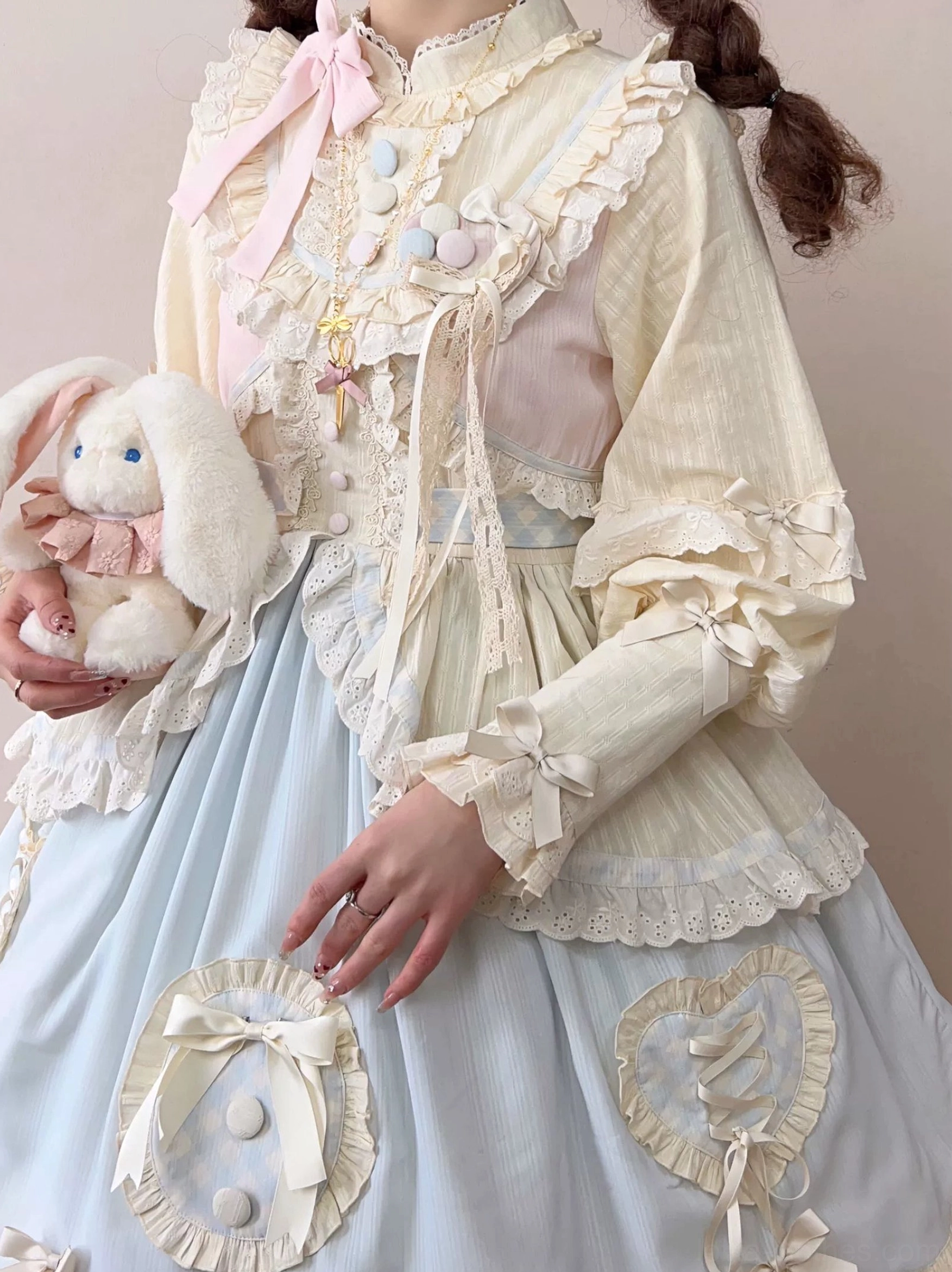 Partial close-up detail of sweet lolita OP dress featuring heart-shaped bow applique on light blue skirt fluffy pom-pom trims delicate lace cuffs vintage brooch accessory plush rabbit