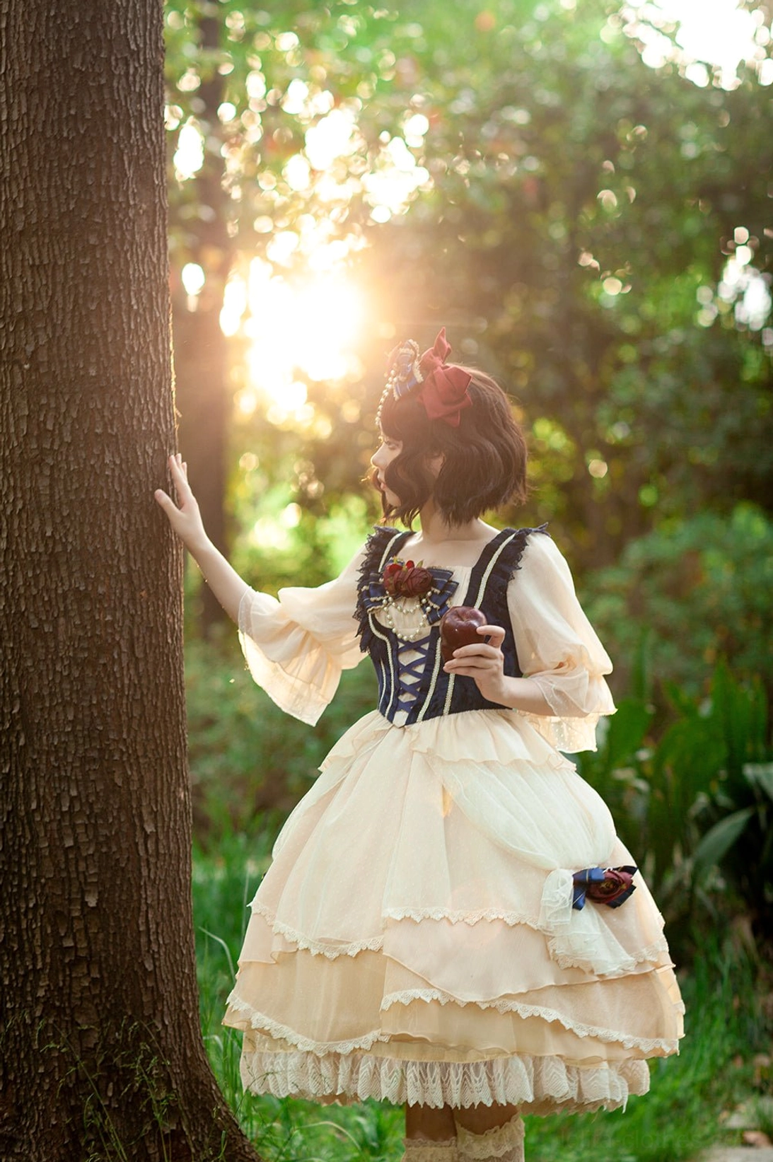 Snow White Lolita OP dress back view showing lace-up corset and layered ruffled skirt with flower accents, model wearing dress leaning against tree in forest sunset scene