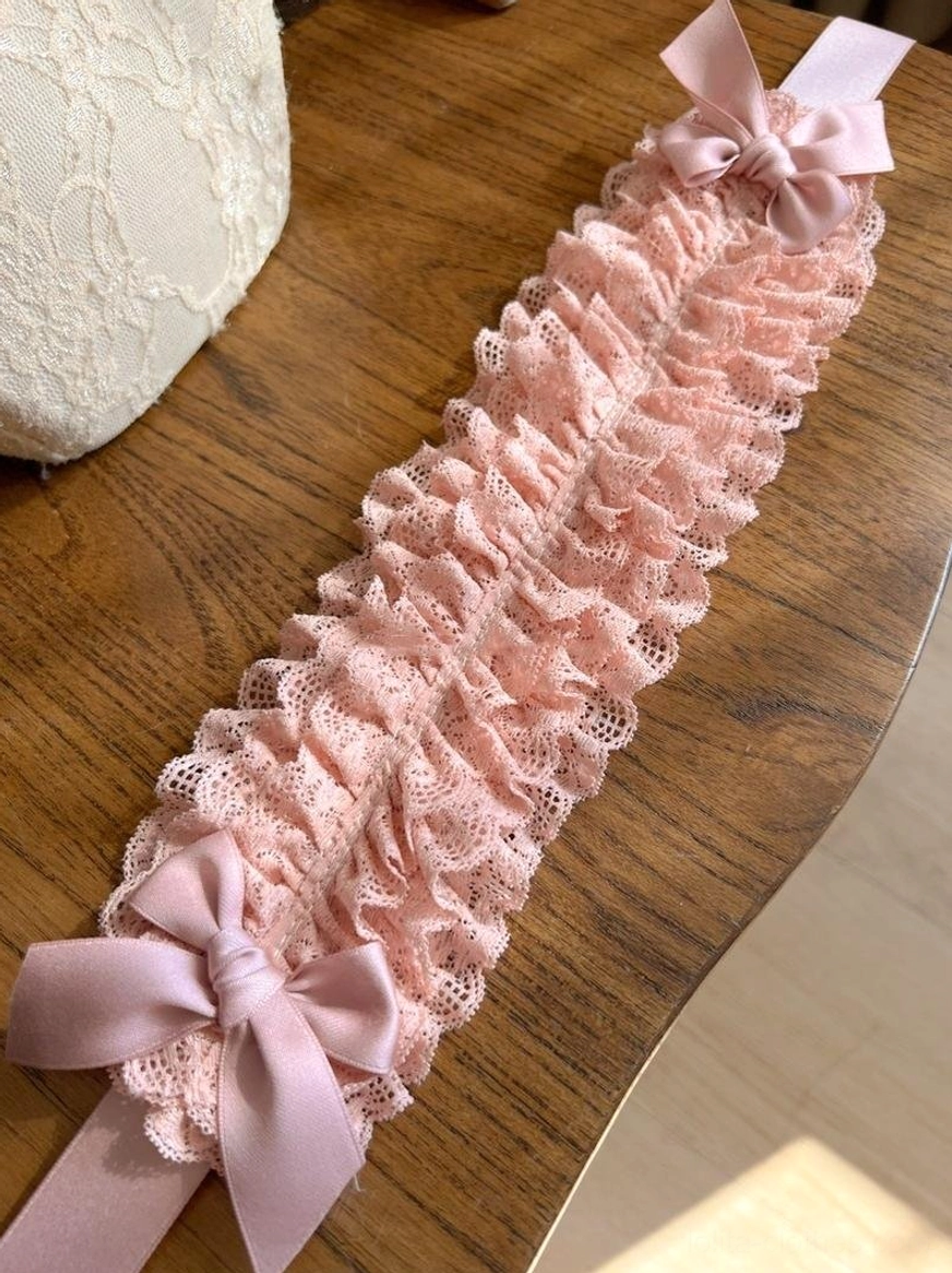 Soft pink lolita lace KC flat lay product shot from overhead, showing ruffled lace texture, two decorative satin bows, and matching ribbon straps