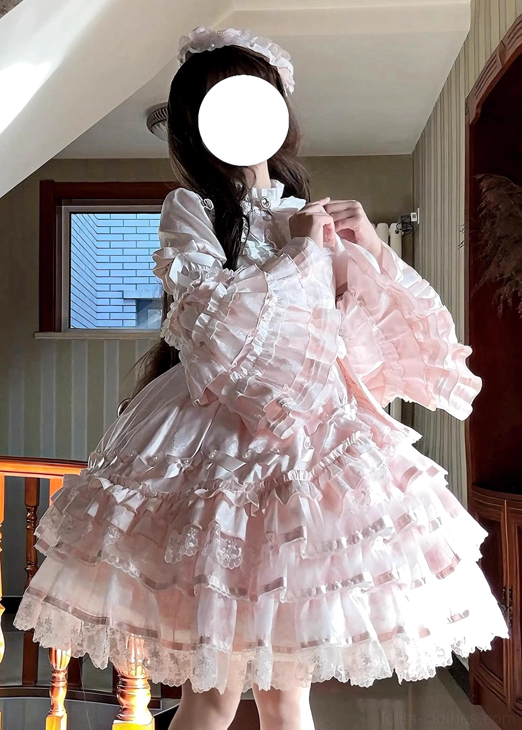 Pastel pink sweet lolita OP dress front view indoor residential setting princess long sleeves sheer tulle layered ruffled skirt lace stand collar model adjusting neckline