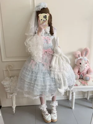 Sky-blue Sweet Lolita Jumper Skirt coordinated with white lace-trimmed princess-sleeved blouse, showcasing tiered tulle skirt overlay, pink satin bow decorations, and white bridal veil hair accessory paired with white platform shoes