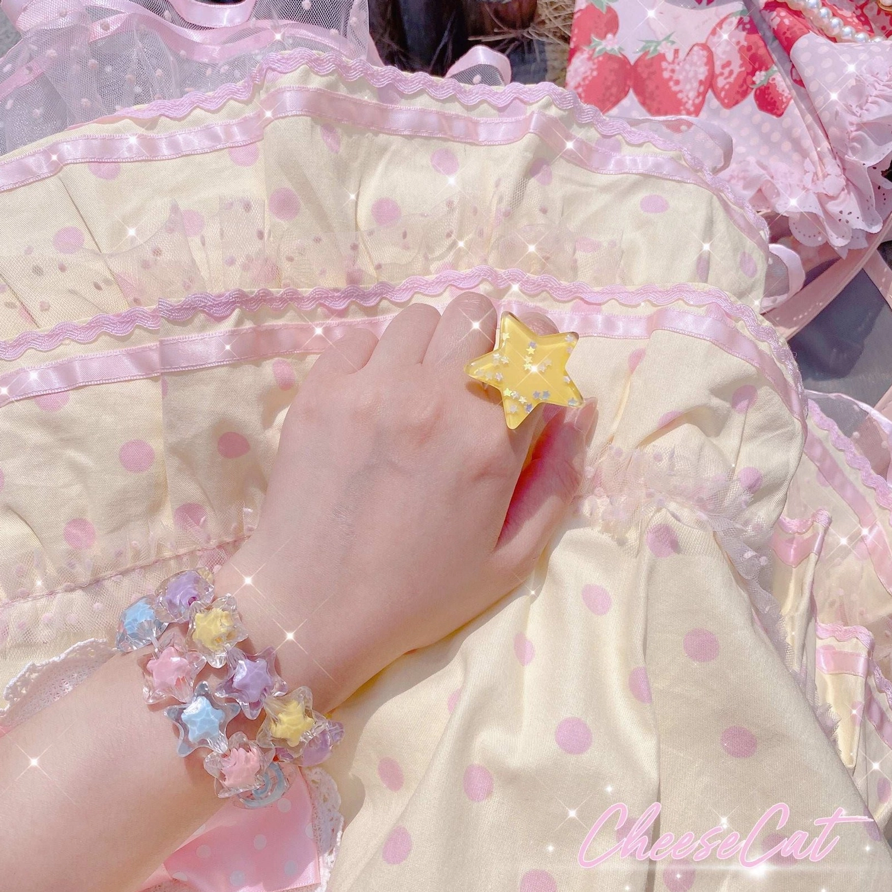 Close-up hand shot of star beaded Lolita bracelet and yellow star resin ring with mixed pastel star beads elastic bracelet design and sparkly glitter surface, photographed against yellow polka-dot dress fabric