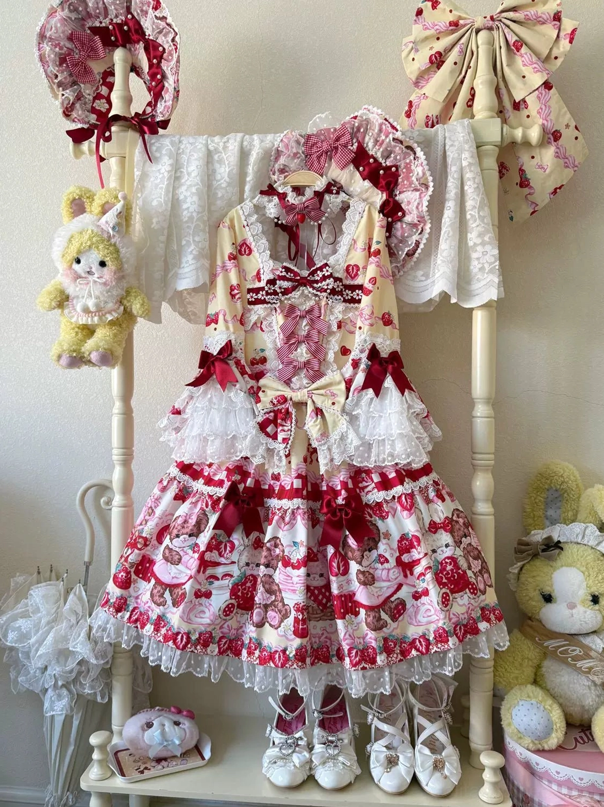 Strawberry bear print lolita OP dress hanging display with white base, red prints, layered lace ruffles, back bow, matching bonnet and hair accessories on boutique rack