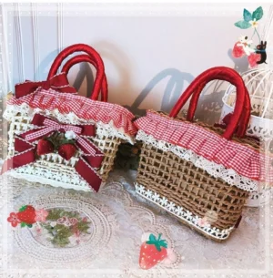 Beige and brown strawberry gingham Country Lolita straw tote bags displayed side by side with red handles and fruit decorations