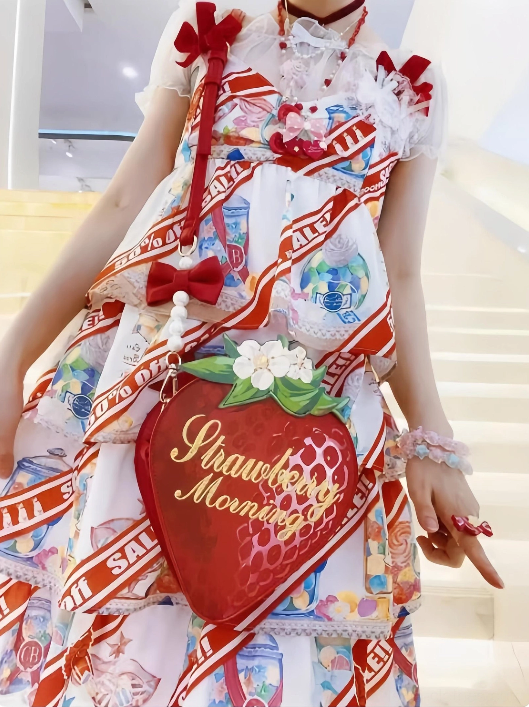 Model wearing strawberry sweet lolita crossbody bag with red-white printed lolita jumpskirt on staircase