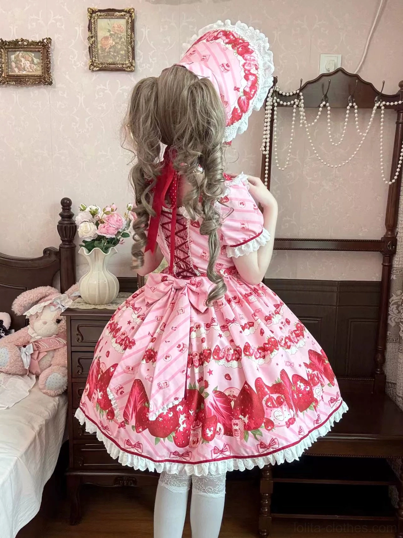 Model wearing strawberry lolita dress back view twin curly hairstyle bonnet with long ribbon lace-up back dress detail vintage bedroom setting full body