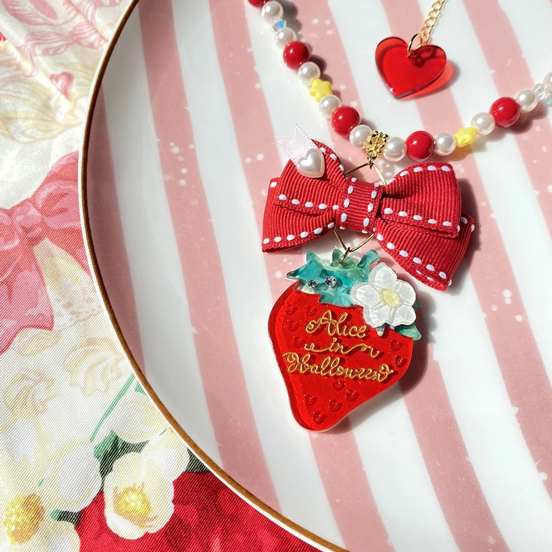 Strawberry lolita necklace accessory with red bow and beaded chain on pink striped plate flat lay