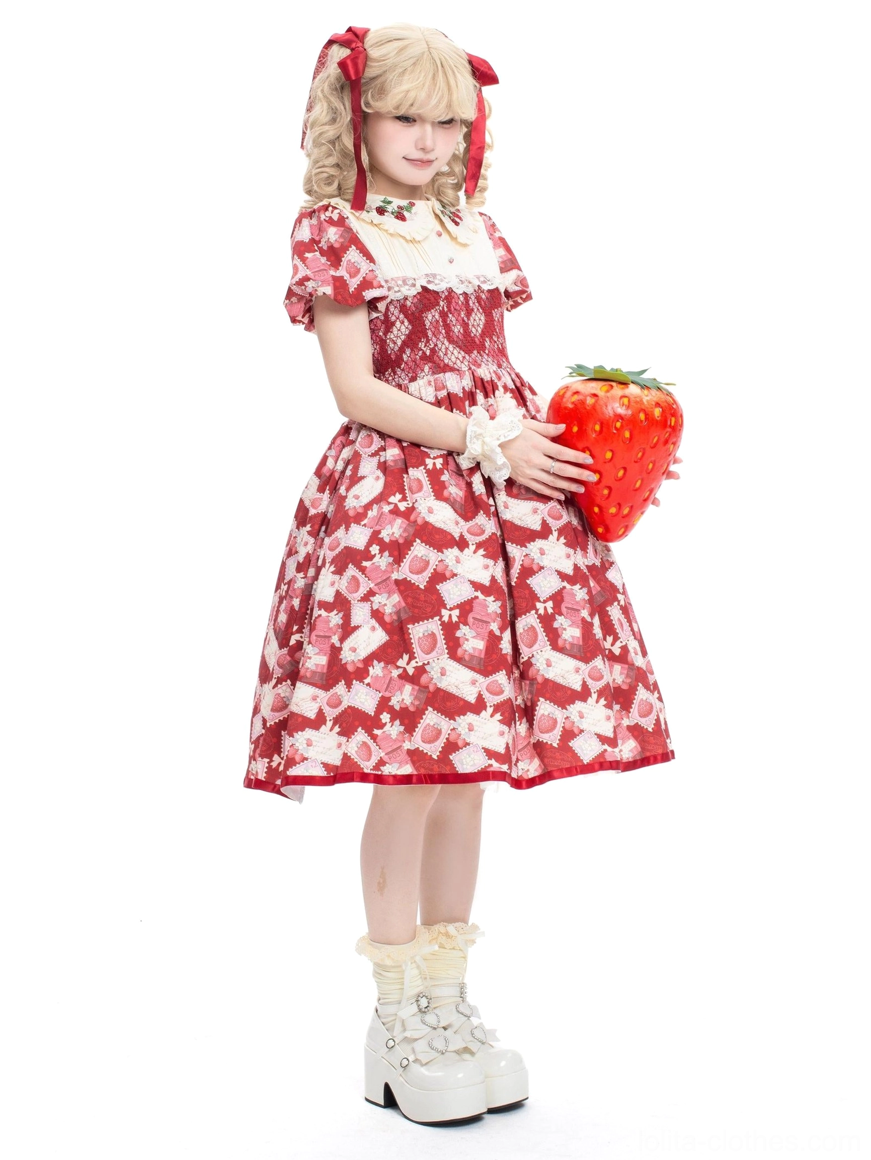 Strawberry print Lolita OP dress side view displaying matching all-over fabric print, decorative wrist cuffs, classic bell-shaped silhouette, model holding giant strawberry prop with twin tails