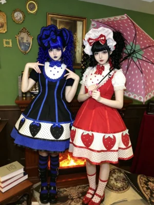 Full front group view of two vintage strawberry Old School Lolita JSK dresses in red and black-blue colorways with lace-trimmed collars and heart-adorned strawberry prints on hemlines
