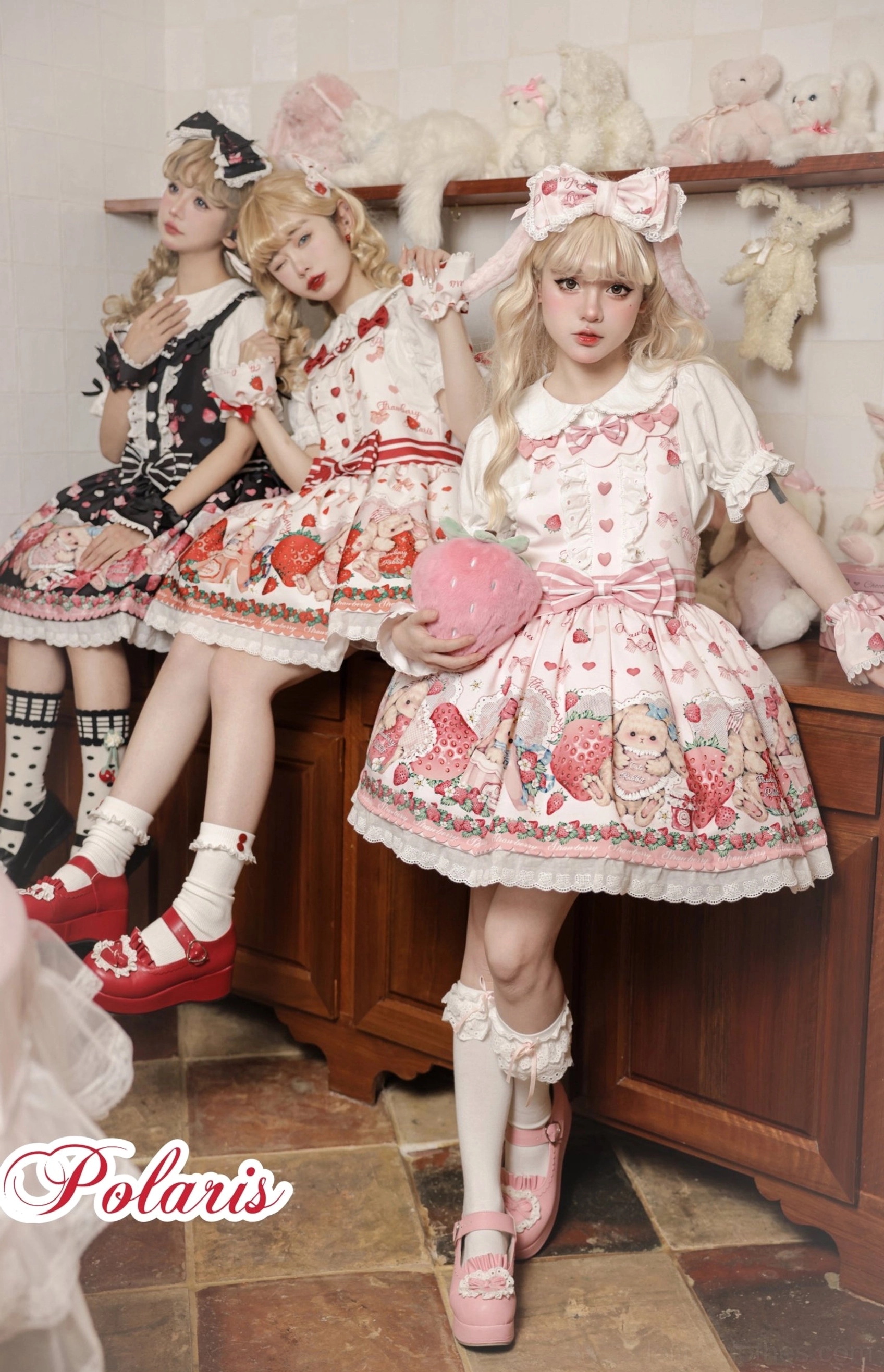Three models wearing strawberry rabbit sweet lolita salopette JSK dresses in pink red and black with lace trim ruffles and bow details in vintage kitchen setting