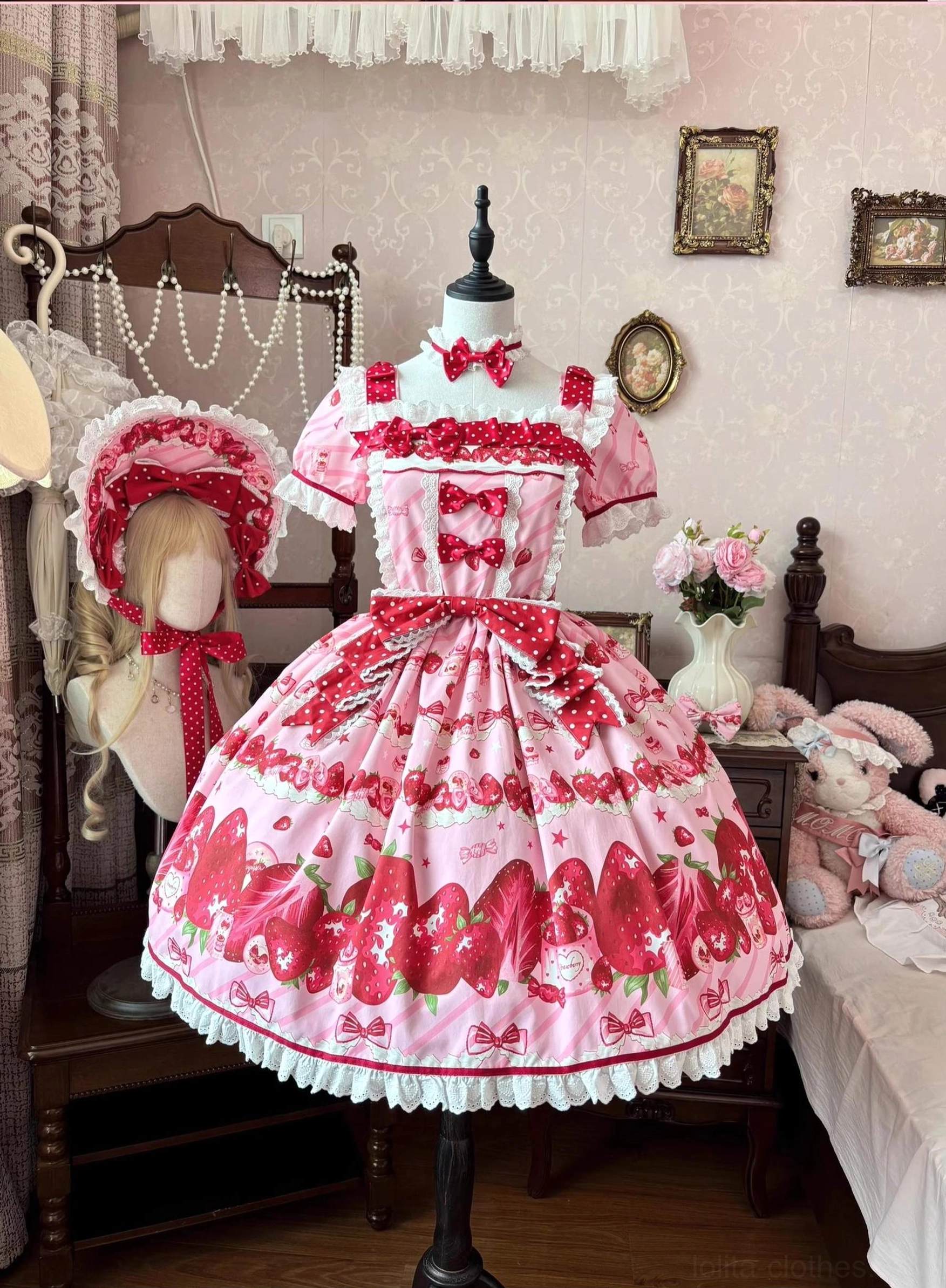 Strawberry sweet lolita OP dress front view on mannequin displaying pink fabric with red strawberry all-over print white ruffled lace hem trim polka dot ribbon waist bow