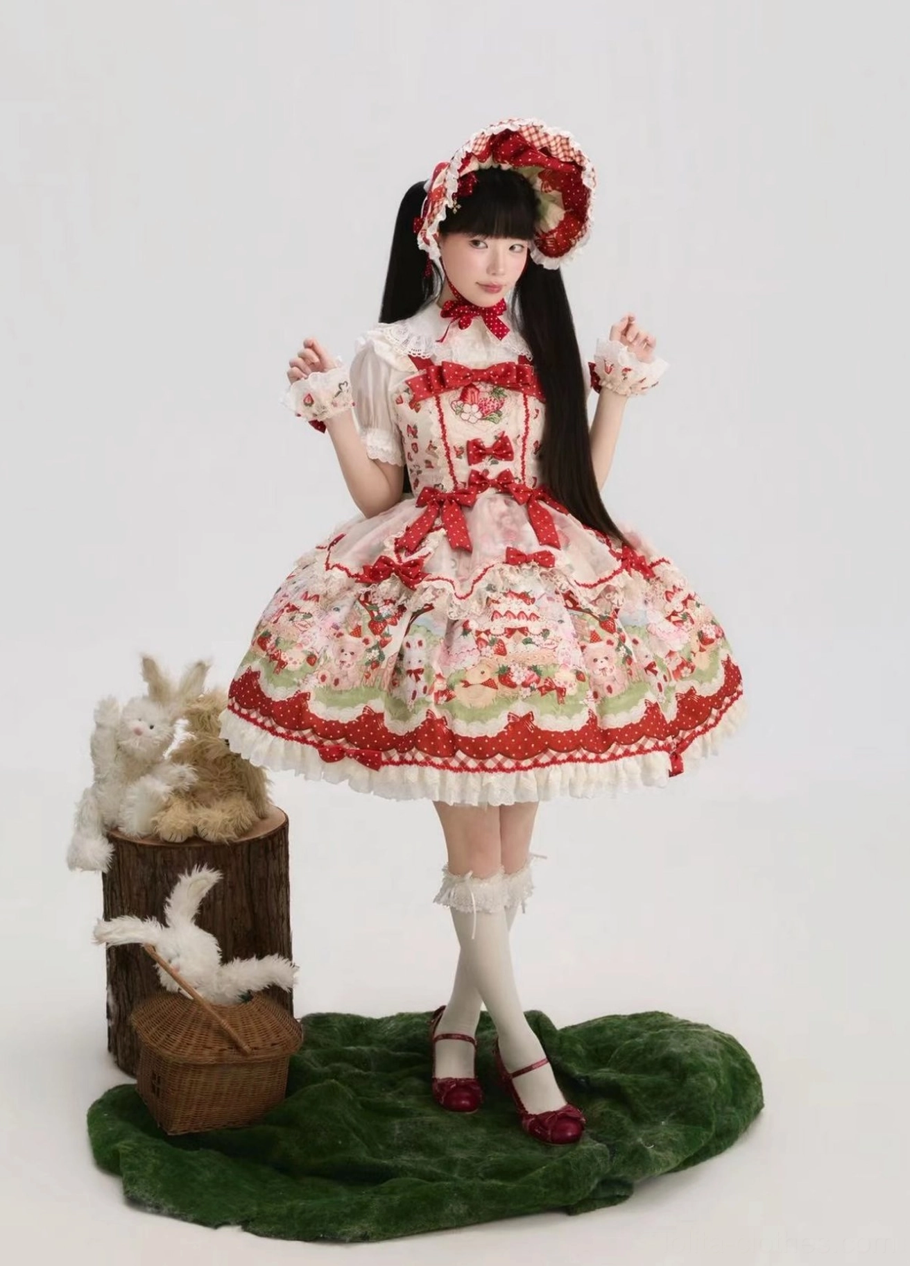 Strawberry tea party sweet Lolita JSK dress front full-body view with matching bonnet, featuring red off-white color scheme, adorable strawberry dessert print with kittens bears and bunnies, ruffled lace hem with polka dot details, and coordinating red bow trims on woodland decor background