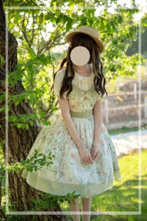 Full-body front view of summer floral lolita OP dress with sage green waistband and A-line skirt, worn with straw hat and lawn background