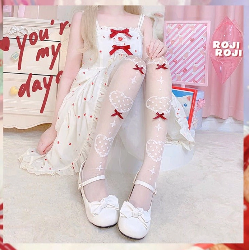 Sitting view of Lolita girl in white heart-print sweet dress wearing sheer knee socks with bow heart motifs and white bow Mary Jane shoes