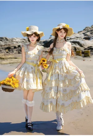 Two models wearing matching sunflower printed classic lolita JSK dresses with tiered ruffled hems and yellow waist ribbons on a seaside beach setting