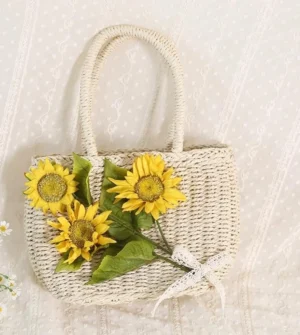 Top front angled view of sunflower decorated woven straw Lolita handbag with ivory lace bow on embroidered lace background