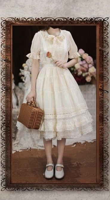 Model wearing vintage-inspired beige Lolita dress with ruffled collar, puff sleeves, tiered skirt and lace hem, styled with Mary Jane shoes, woven handbag and rose accessory