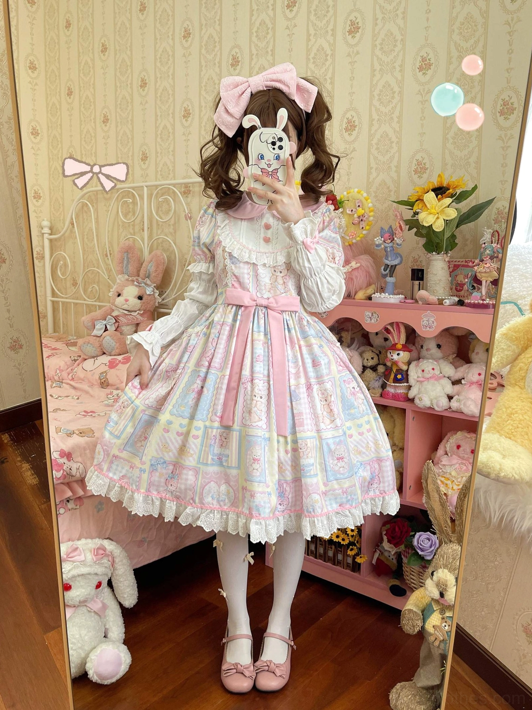 Mirror front full-body shot of Sweet Bunny Bear Lolita OP dress featuring large pink hair bow, pastel patchwork bunny and bear print, pink waist sash, lace skirt trim, and plush bedroom display