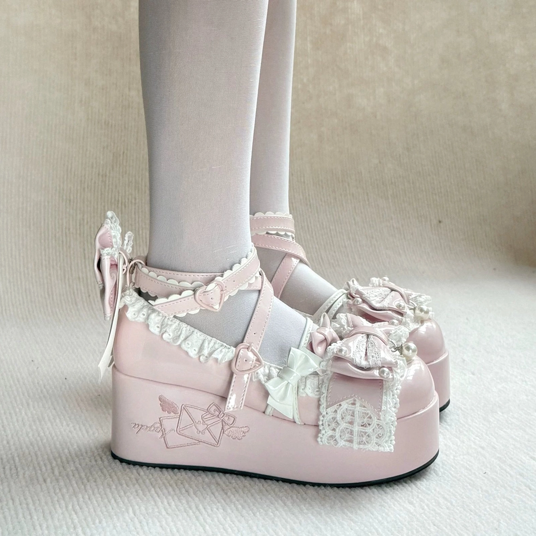 Sweet Dream Letter platform shoes close-up of crisscross ankle strap with heart-shaped buckle, ruffled vamp with pearl embellishments, and glossy patent leather surface detail