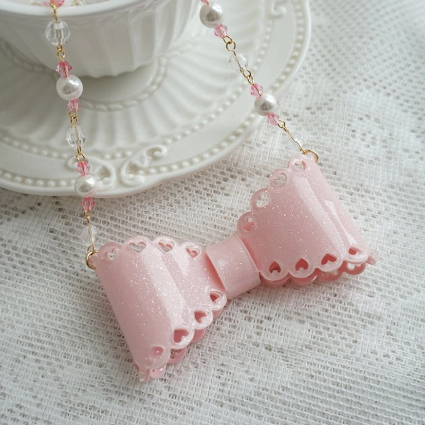 Handmade sweet lolita beaded pink glittery bow necklace with scalloped resin edges and pearl beaded chain on vintage lace tablecloth with porcelain teacup