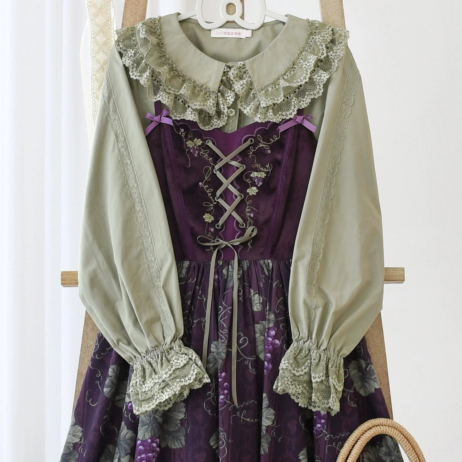Sweet Lolita blouse and purple embroidered JSK dress coordinated set displayed on wooden clothing rack, featuring sage green top with lace ruffled collar and cuffs, lantern long sleeves, and corset lace-up front detail