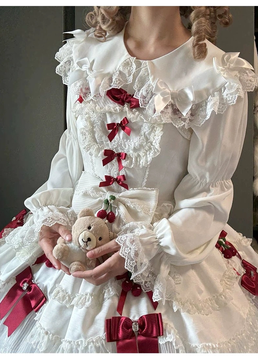 Close-up front upper body view of sweet Lolita blouse and full skirt with vertical red bow trims, large side red bows, and delicate lace appliques worn by model with teddy bear