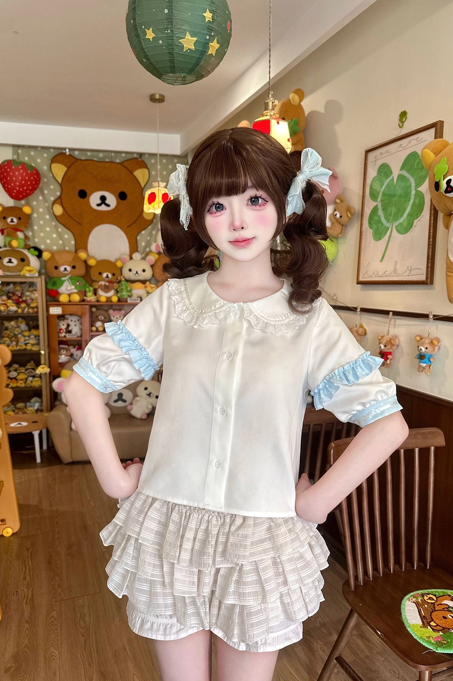 Matching Sweet Lolita daily blouse and skirt set front full-body view worn by model in plush toy bedroom, white doll collar short-sleeve blouse with plaid tiered ruffled mini skirt coordination