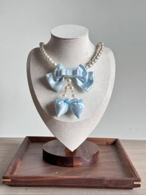 Light blue sweet lolita polka dot bow pearl choker necklace with dangling bow charm on bust display wooden tray