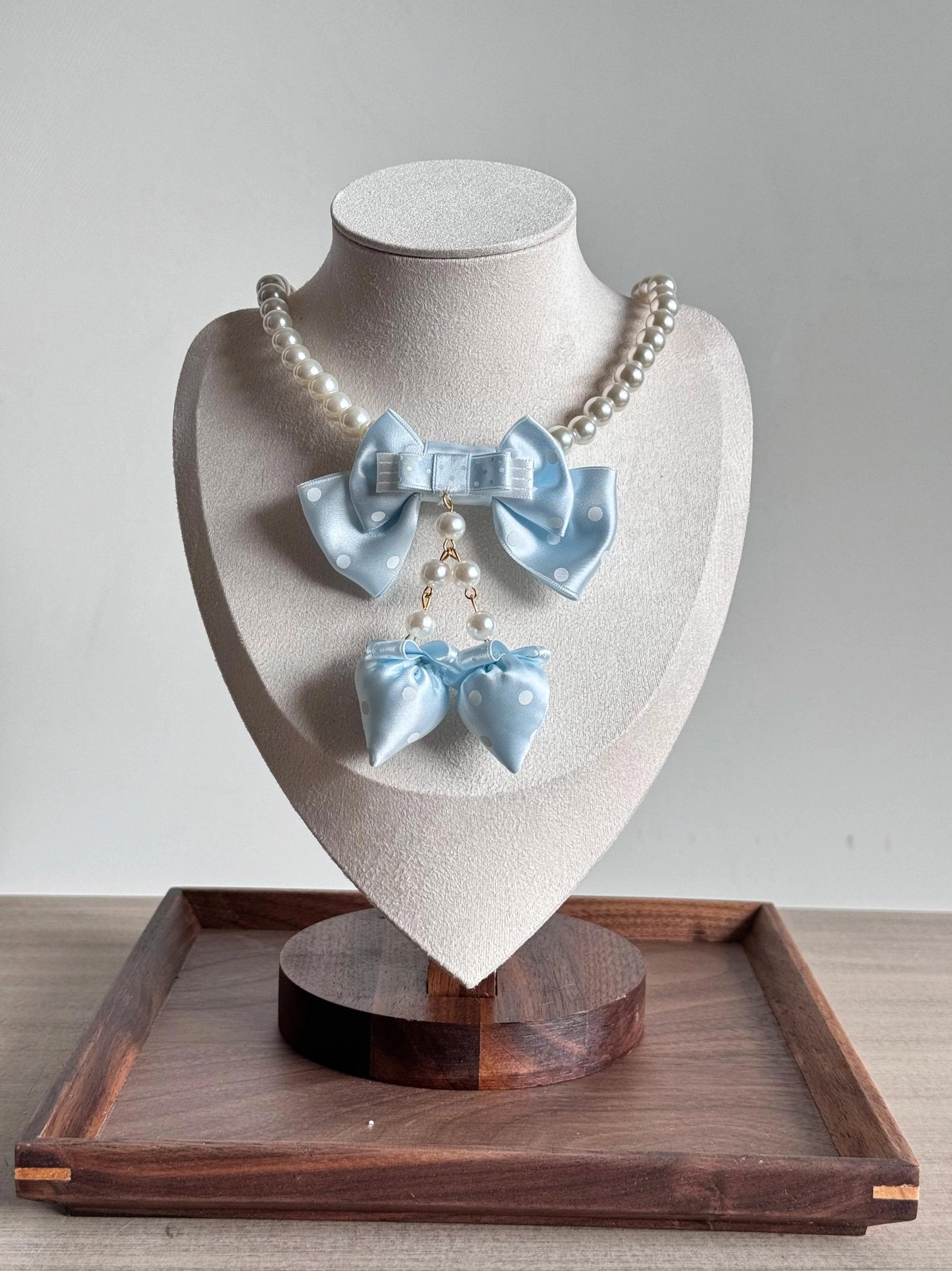 Light blue sweet lolita polka dot bow pearl choker necklace with dangling bow charm on bust display wooden tray