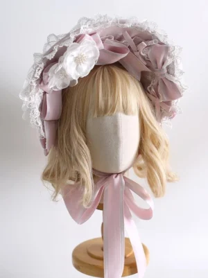 Sweet lolita pink satin bonnet headdress with tiered white ruffled lace trim and detachable burnt-edge silk flowers, front three-quarter view on blonde wig mannequin