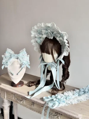 Pastel blue sweet lolita bonnet accessory set with ruffled lace trims and long satin ribbon ties displayed on vintage carved wooden dressing table