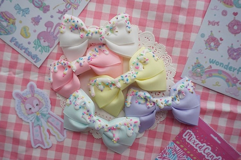 Five pastel color sweet lolita cream cake bow hair clips arranged on lace doily with decorative stickers overhead view