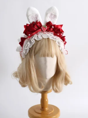 Sweet lolita bunny ear headpiece KC with fluffy white ears, red satin bow, and strawberry charm detail worn on blonde wig display stand - front full view