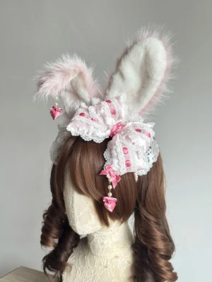 Pink polka dot sweet lolita bunny ear hair accessory left side three-quarter view, fuzzy white-pink rabbit ears, lace-trimmed bow, pink heart drop pendant on mannequin with twin-tailed wig